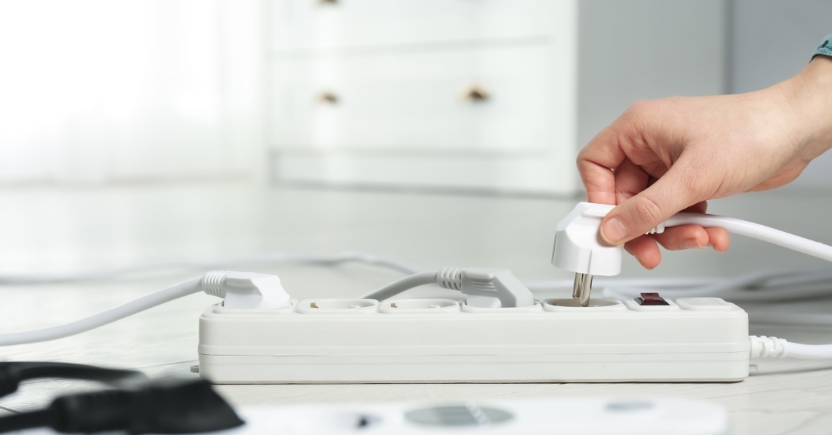 An individual plugging a white electrical cord into a power strip with multiple outlets on a desk surface.