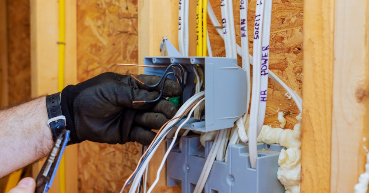 A gloved electrician connects wiring inside an unfinished wall junction box during a residential electrical installation.