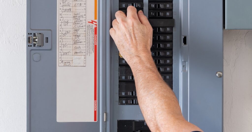 Hand resetting a circuit breaker inside a residential electrical panel with labeled circuits and multiple breaker switches.