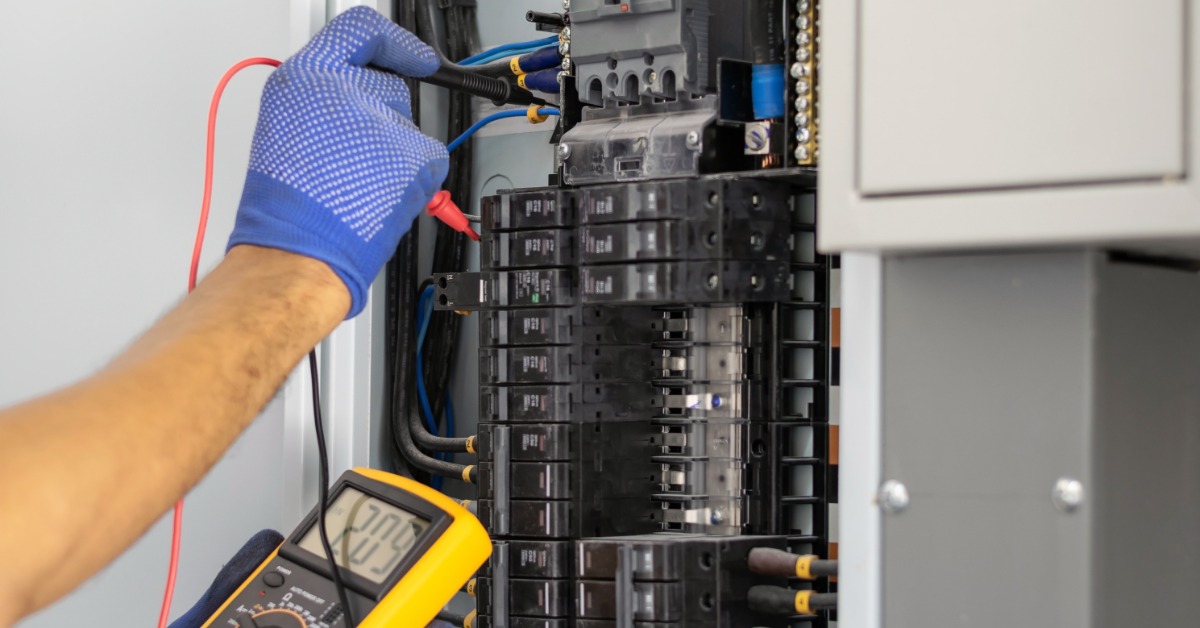 Electrician uses a multimeter to test wiring and circuit breakers inside an open residential electrical panel.