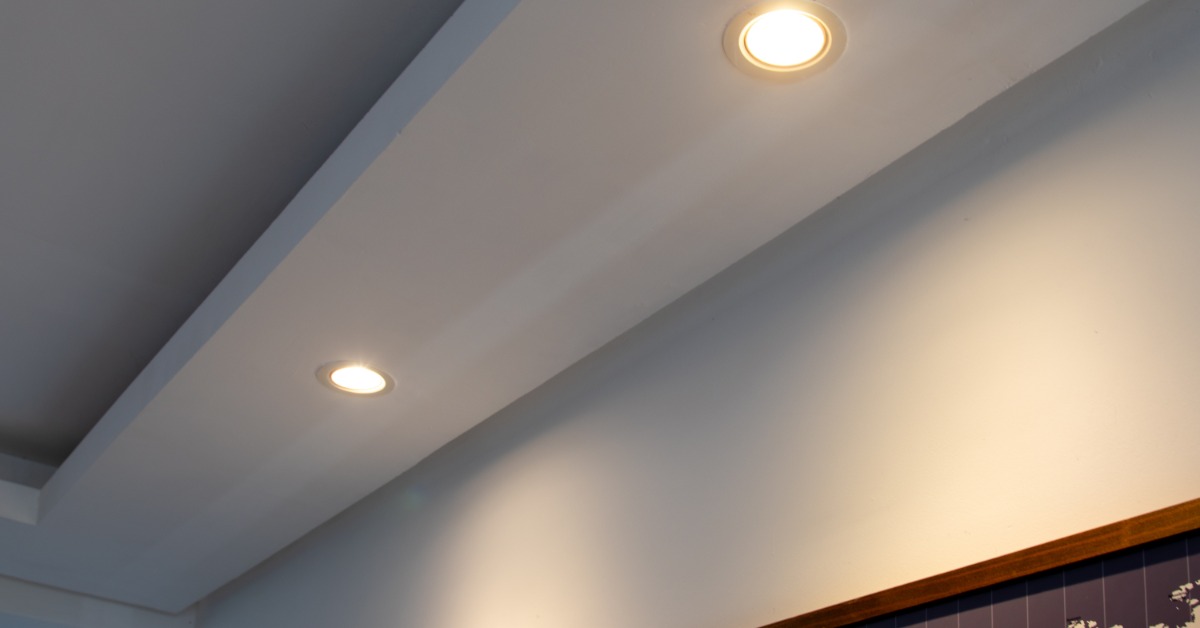 Two illuminated recessed ceiling lights cast warm light across a white soffit and adjacent light gray wall.